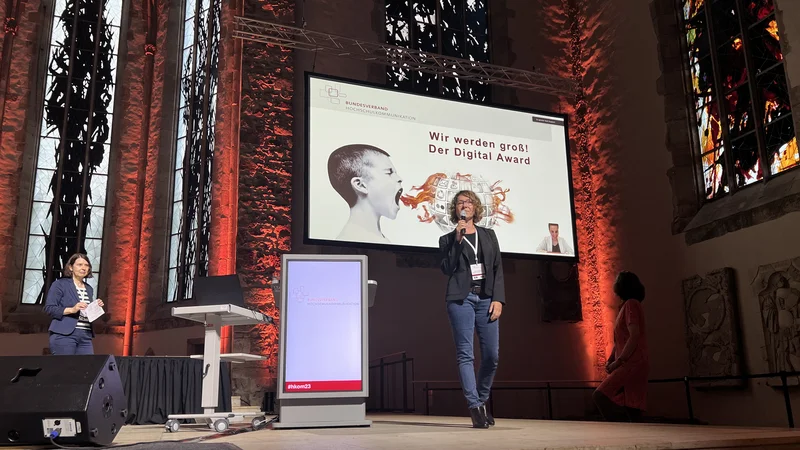 Eine Frau redet vor einer gro&szlig;en Leinwand auf einer B&uuml;hne