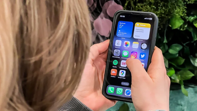 Blick über die Schulter einer Person, die ihr Smartphone in der Hand hält und die Startoberfläche ihres Handys bedient.